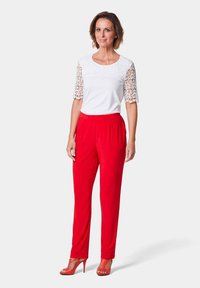 Haut blanc avec des manches en dentelle, associé à un pantalon plissé rouge et des talons rouges à lanières. Tissu lisse avec un détail en dentelle complexe.
