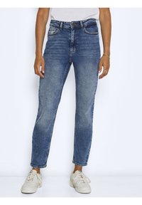 Blaue Jeans im Slim-Fit-Schnitt, mittelhoher Bund, Fünf-Taschen-Design und dezente Ausbleichungen. Kombiniert mit weißen Sneakers.