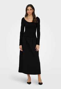 Sort langærmet top med rund halsudskæring parret med en sort maxiskirt. Stoffet ser blødt ud med et enkelt, udekoreret design.