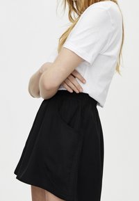 Jupe en tissu noir avec une taille élastique et une poche latérale, associée à un t-shirt blanc uni à manches courtes. Design simple et décontracté.