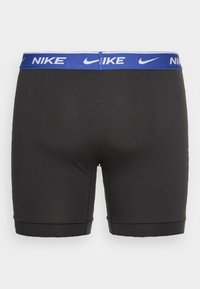 Sorte atletiske shorts med en blå elastisk talje, der har Nike-logoet i hvidt. Stoffet ser glat og tætsiddende ud.