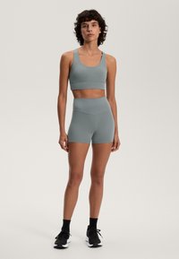 Športová podprsenka a vysoké nohavice z mäkkej šedej textílie, bezšvový dizajn, priliehavý strih a hladká štruktúra. V kombinácii s čiernymi športovými topánkami.