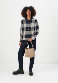 Karierte Hemdbluse in Beige und Marineblau, schwarze Kampfstiefel, marineblaue Hose und eine sandfarbene Wildleder-Bucket-Bag. Glattes Material mit langen Ärmeln.