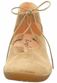 Scarpa in suede beige con design ritagliati, allacciatura frontale e punta arrotondata liscia. La suola è di un nocciola chiaro, creando un sottile contrasto.