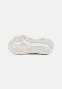Semelle de chaussure de sport blanche avec des motifs de grip texturés et le logo Saucony au centre, présentée sur un fond blanc uni.