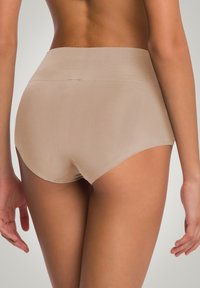 Beżowa, bezszwowa bielizna wysoka w talii o gładkiej fakturze i zaokrąglonych otworach na nogi. Minimalistyczny design bez widocznych szwów czy wzorów.