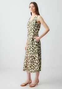 Beige en olijfgroene jurk met bloemmotief, kniehoog met V-hals, mouwloos ontwerp en zijzakken. Glad, lichtgewicht stof.
