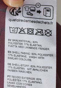 Vaskeanvisning og sammensætning på et let stof: 83% polyester, 17% elastan. Flersproget tekst.