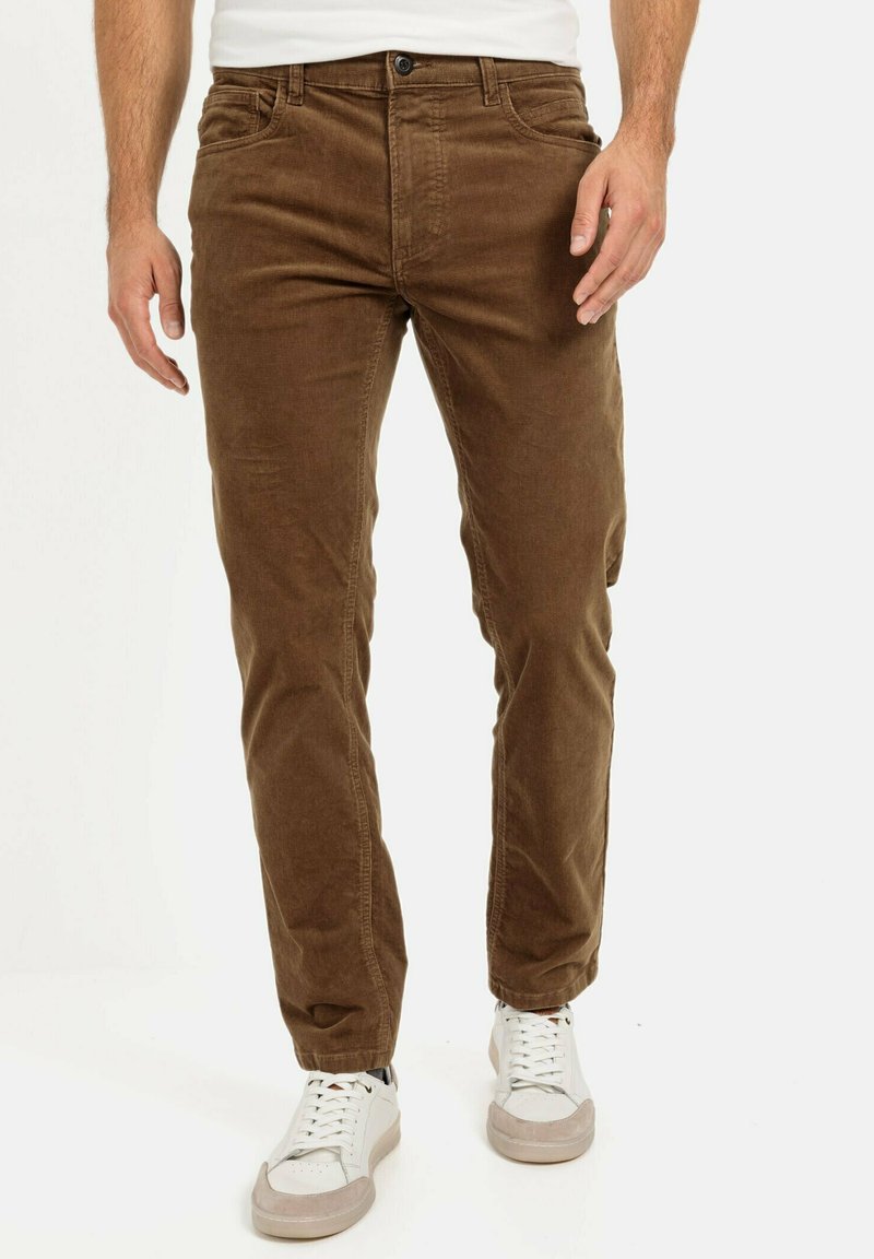 Pantalon en velours côtelé marron avec une coupe slim, doté de poches avant, de passants de ceinture et de coutures contrastées. Associé à des baskets blanches.