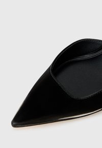 Mustat, teräväkärkiset ballerinat, joissa on sileä ja kiiltävä pinta sekä avoimet sivut. Sisältää pehmeän sisävuoren ja minimalistista yksityiskohtaa.