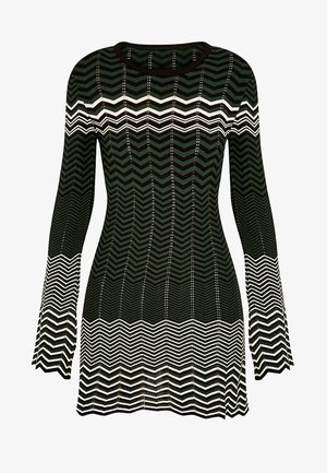 Mustavalkoinen chevron-kuvioitu pitkähihainen neulepusero, jossa levenevät hihansuut ja istuva siluetti.