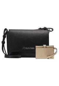 Černá crossbody taška Calvin Klein s nastavitelním popruhem a béžový kožený držák na karty s zápěstním popruhem, obě s embosovaným logem Calvin Klein.