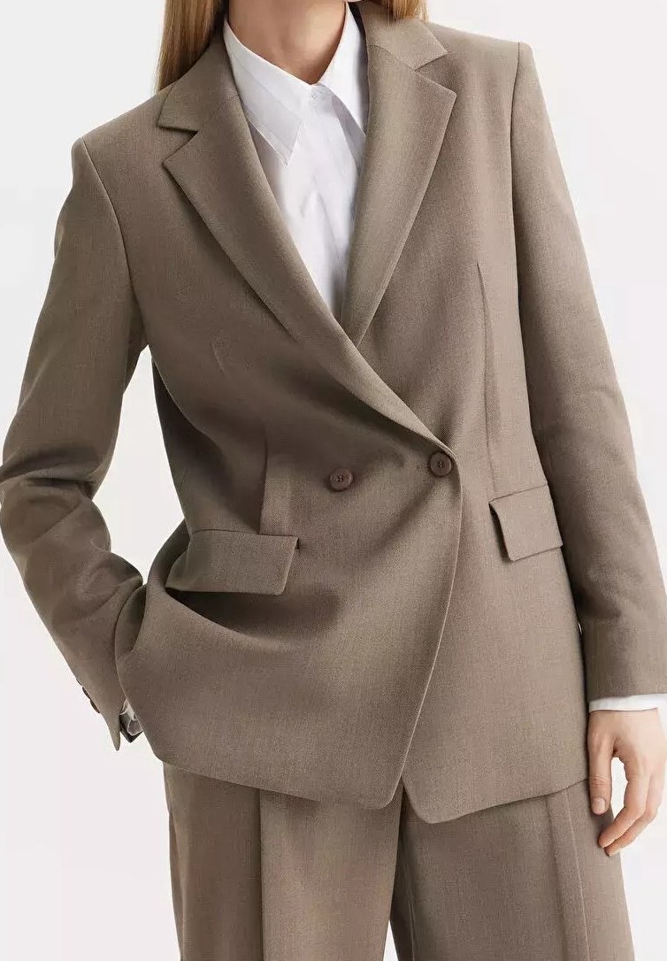 Femme portant un blazer croisé taupe et un pantalon assorti avec une chemise blanche à col en dessous.