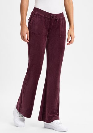 Bordeauxfarbene, aus weichem Samt gefertigte, ausgestellte Lounge-Hose mit einem Kordelzugbund und zwei vorderen Taschen. Kombiniert mit weißen Sneakers.