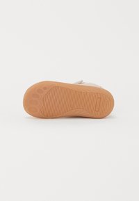 Sko såle i beige gummi med teksturert grep, med avrundet hæl og poteavtrykk-design. Flatt med horisontale riller for bedre grep.