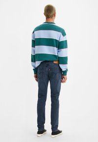 Green and light blue striped sweater with a high neckline, paired with dark blue jeans. Features a rectangular back pocket design.