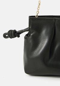 Černá kožená taška s designem s nabíraným efektem, zavazováním na uzel a zlatým řetízkovým popruhem. Hladká textura zdůrazňuje její elegantní vzhled.
