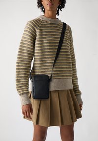 Stribet striktrøje i beige, sennepsgul og grå nuancer med en ribbet halsudskæring, parret med en plisseret beigefarvet nederdel og en lille sort crossbody taske.