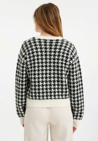 Černobílý svetr pletený s kostkovaným vzorem houndstooth, s žebrovanými manžetami a lemem, s krátkým střihem a měkkou texturou.