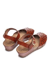 Brown leather sandals with cutout designs, adjustable ankle strap, textured footbed, and wedge sole, featuring a light tan base.