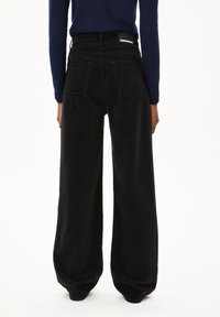 Schwarze Cordhose mit weitem Bein, hoher Taille, zwei Gesäßtaschen und einem Etikett am Bund. Weicher Stoff und lockere Passform.