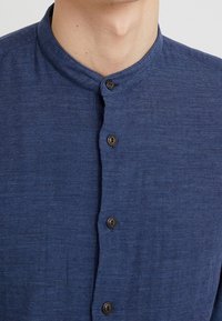 Niebieska koszula na guziki z kołnierzem mandaryńskim, teksturowaną tkaniną i brązowymi guzikami na froncie. Elegancki, smukły design.