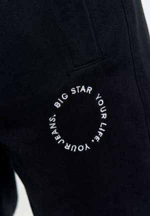 Pantaloni jogger neri realizzati in morbido tessuto con un logo circolare ricamato. Vita elasticizzata con dettaglio delle tasche.