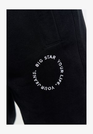 Czarne spodnie dresowe wykonane z miękkiego materiału, z haftowanym okrągłym logo. Elastyczna talia z detalem kieszeni.