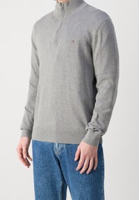 Felpa grigia con zip e collo alto, realizzata in tessuto morbido. Presenta polsini e orlo a coste, con un piccolo logo sul petto.