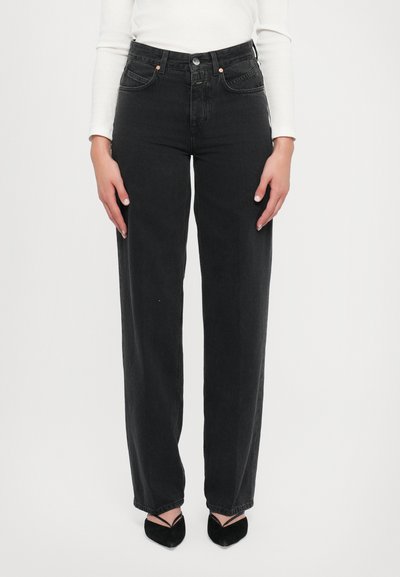 Hochtaillierte schwarze Jeans aus Denim mit geradem Bein, ausgestattet mit Vorderaschen und einem Knopfverschluss, kombiniert mit schwarzen Absatzschuhen.