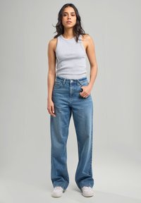 Top sin mangas gris claro combinado con jeans de denim azul de pierna ancha. Los jeans presentan una cintura alta y un lavado desvaído, con detalles de costura sutiles.