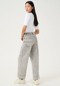 Faded gray wide-leg jeans with a high waist, featuring two back pockets and rolled cuffs. Paired with a white fitted top and light sneakers.