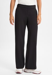 Zwarte, high-waisted broek met een gladde textuur, recht model, zijzakken en een subtiele glans. Gestyled met witte sneakers.