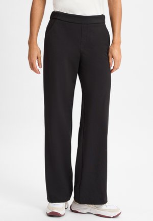 Zwarte, high-waisted broek met een gladde textuur, recht model, zijzakken en een subtiele glans. Gestyled met witte sneakers.