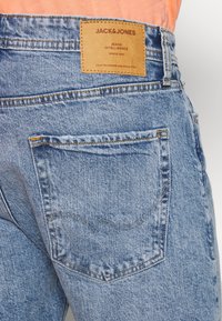 Jean de mezclilla azul con un parche de cuero que dice "JACK & JONES". Incluye un bolsillo trasero con costuras en contraste y tela texturizada.