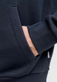 Laivastonsininen collegepaita, jossa on kengurutasku, resorireunuksiset hihat ja helma. Sileä pinta, jossa ompeluaita ja pieni merkkilappu.