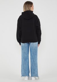 Felpa nera con cappuccio e taglio comodo, abbinata a jeans blu chiari a gamba larga. Il tessuto sembra morbido con polsini e orlo a costine.