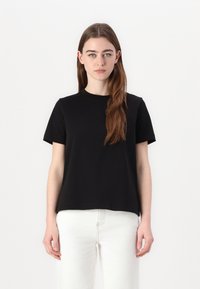 Svart kortermet T-skjorte i vanlig passform, laget av myk bomull. Har rund hals og jevn tekstur, kombinert med hvite jeans.