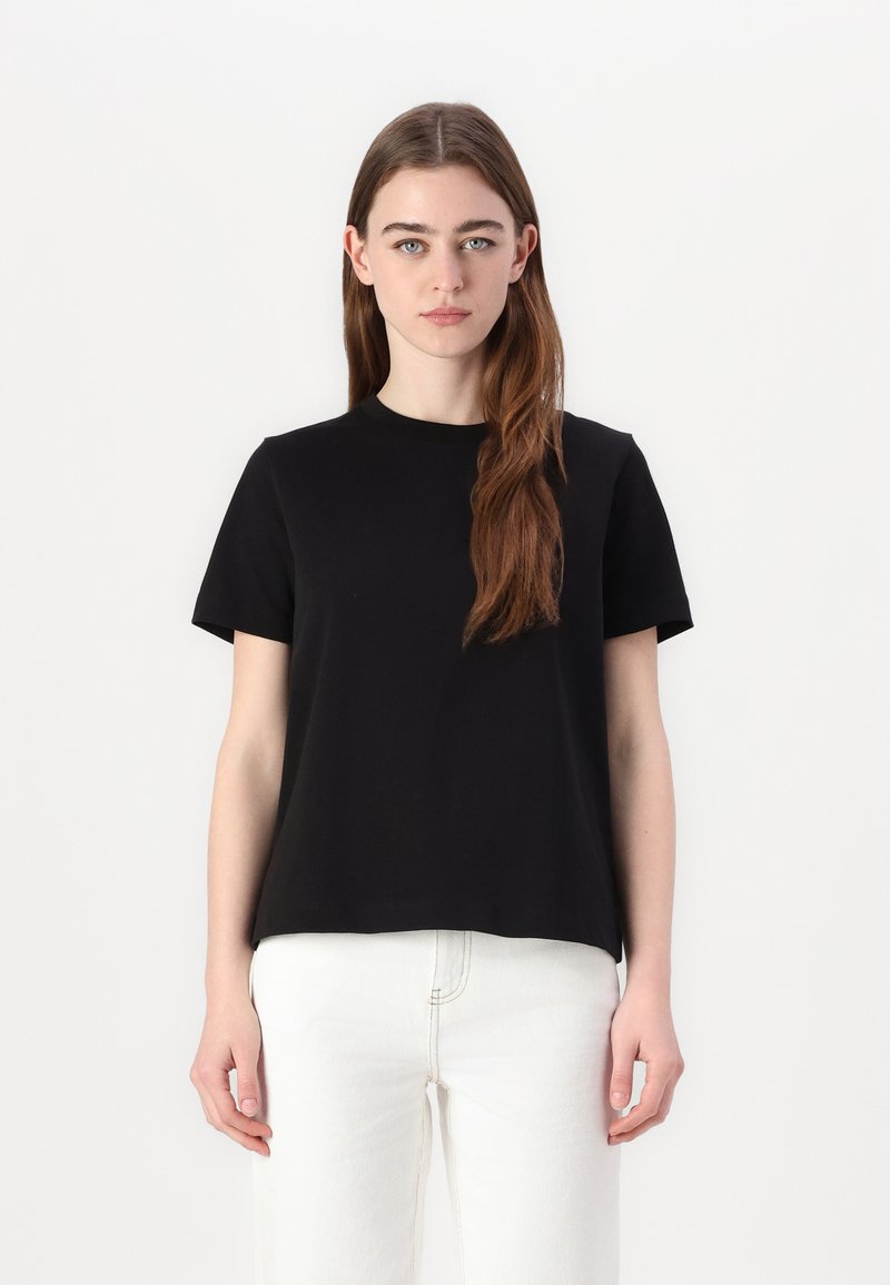 Svart kortermet T-skjorte i vanlig passform, laget av myk bomull. Har rund hals og jevn tekstur, kombinert med hvite jeans.