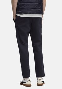 Marineblå sweatpants i blødt stof med tætsiddende ben, udstyret med sidelommer og en glat tekstur. Sammen med hvide og sorte sneakers.