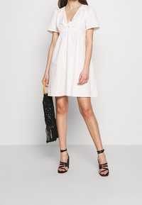 Vit kort klänning med v-ringning och korta puffärmar, med en samlad midja. Tillsammans med svarta klacksandaler med remmar och en svart väska.