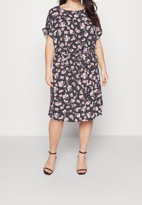 Kukallinen mekko tummansinisellä pohjalla, jossa on vaaleanpunaisia ja valkoisia kukkia, lyhyet hihat, rento malli ja kiristettävä vyötärö. Yhdistetty mustiin remmisandaaleihin.