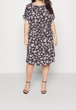 Bloemenjurk in donkerblauw met roze en witte bloemen, korte mouwen, een ontspannen pasvorm en een trekkoord in de taille. Gecombineerd met zwarte sandalen met banden.