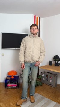 Casaco puffer de corduroy bege com gola alta, design acolchoado e fecho de cremalheira. Combinado com jeans azul claro e botas castanhas.