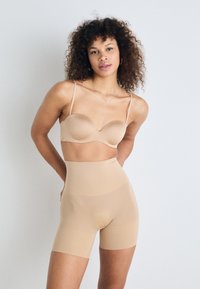 Sutien bej fără cusături și pantaloni scurți cu talie înaltă, realizati dintr-un material neted și elastic, având bretele subțiri și un design ajustat.