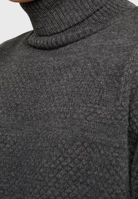 Tumakke tummanharmaa kaula-aukollinen neulepusero, jossa on teksturoitu neulekuvio. Sisältää ribbireunan kauluksessa ja vartalossa sekä tasaisen kudonnan.