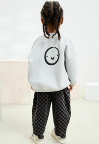 Grauer Kapuzenpullover mit einem schwarzen Smiley-Gesicht-Design auf dem Rücken; karierte schwarz-graue Baggy-Hosen; cremefarbene Sneakers.