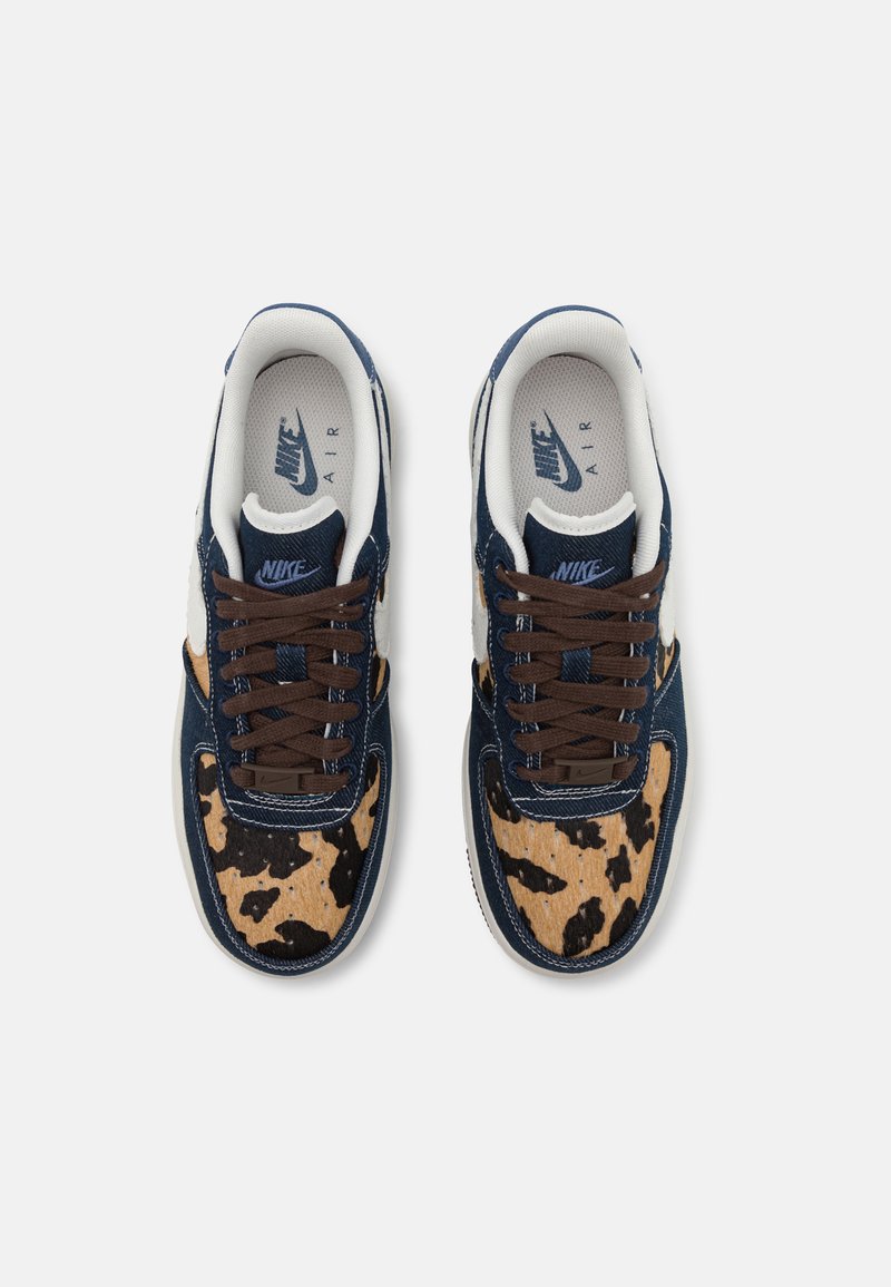 Nike Air Sneakers mit einem dunkelblauen Obermaterial, braunen Schnürsenkeln und einer beigen, gemusterten Zehenpartie mit schwarzen Flecken. Strukturierter Stoff fügt zusätzliche Details hinzu.