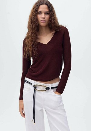 Burgundy long-sleeve top with a V-neck, paired with white trousers featuring a knotted black belt and gold hardware. Smooth texture, fitted design.