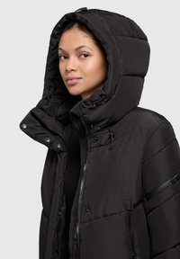 Czarna pikowana kurtka z dużym, grubym kapturem, zatrzaskami, zamkiem błyskawicznym i gładką, zewnętrzną teksturą. Posiada kieszenie z przodu i z boku.
